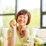 woman surrounded by healthy foods holds and apple and smiles